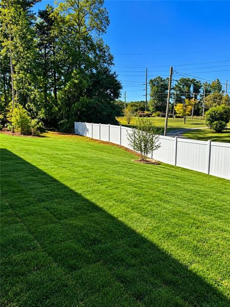 Expansive lawn area with a white privacy fence and mature perimeter trees