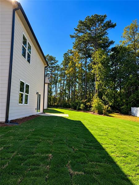 Expansive lawn with mature trees and a white privacy fence